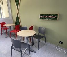 Ambiente com mesas e cadeiras com um letreiro na parede, escrito "Sala da Família" em neon
