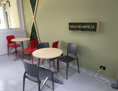 Ambiente com mesas e cadeiras com um letreiro na parede, escrito "Sala da Família" em neon