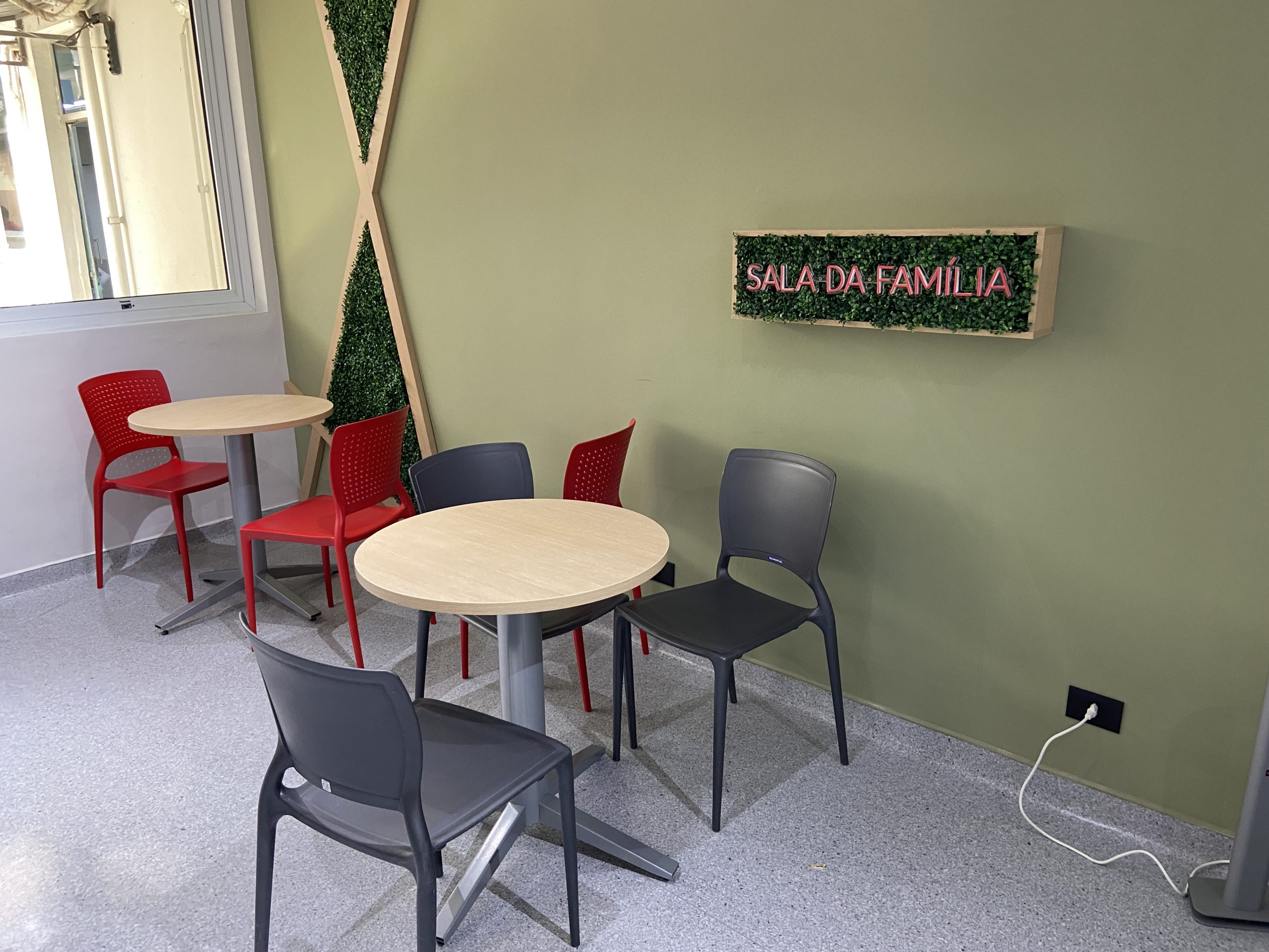 Ambiente com mesas e cadeiras com um letreiro na parede, escrito "Sala da Família" em neon