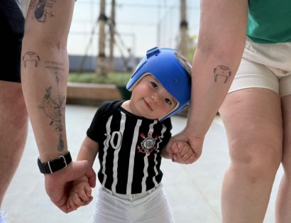 Bebê com o capacete abraçado no braço dos pais, mostrando a tatuagem de capacete