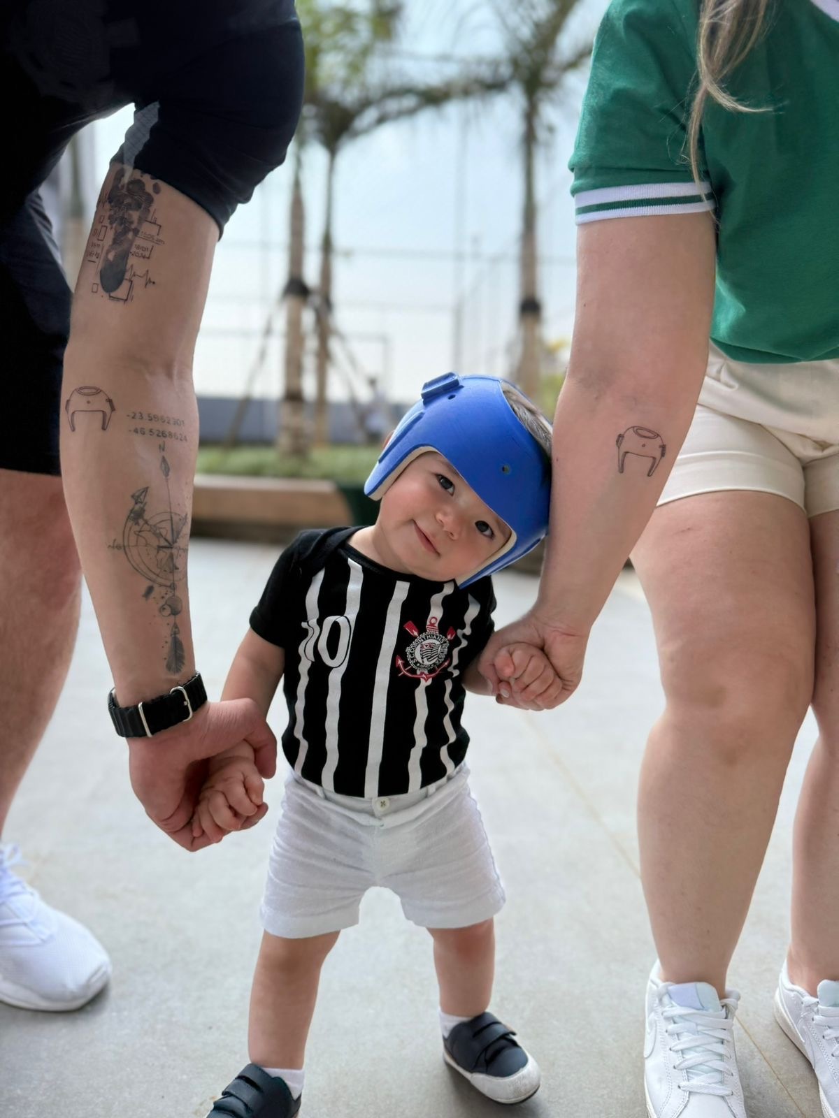 Bebê com o capacete abraçado no braço dos pais, mostrando a tatuagem de capacete