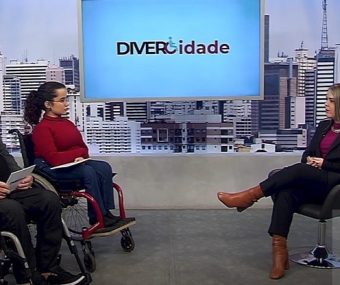 Dra. Ana Rita Donati, uma mulher branca e loira, conversa com os apresentadores do programa Divercidade, ambos cadeirantes, em um estúdio da Rede Cãmara de São Paulo, sobre a saúde da mulher com deficiência.