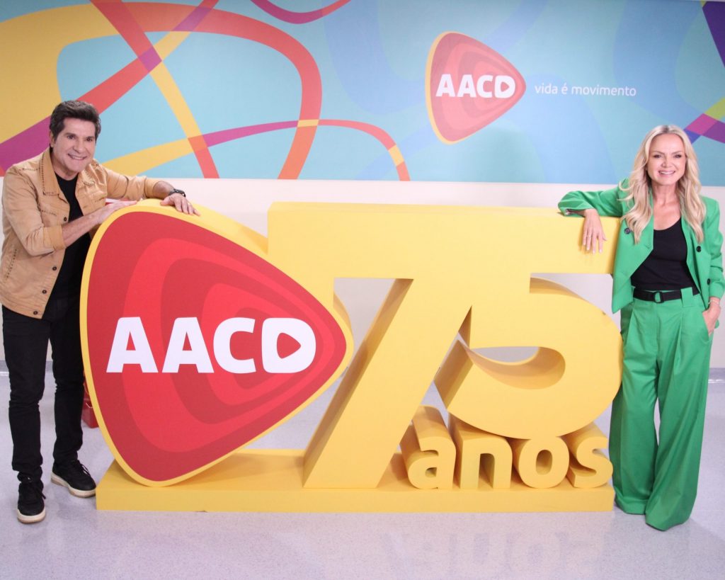 Eliana e Daniel, padrinhos do Teleton, posam no totem de 75 anos da AACD