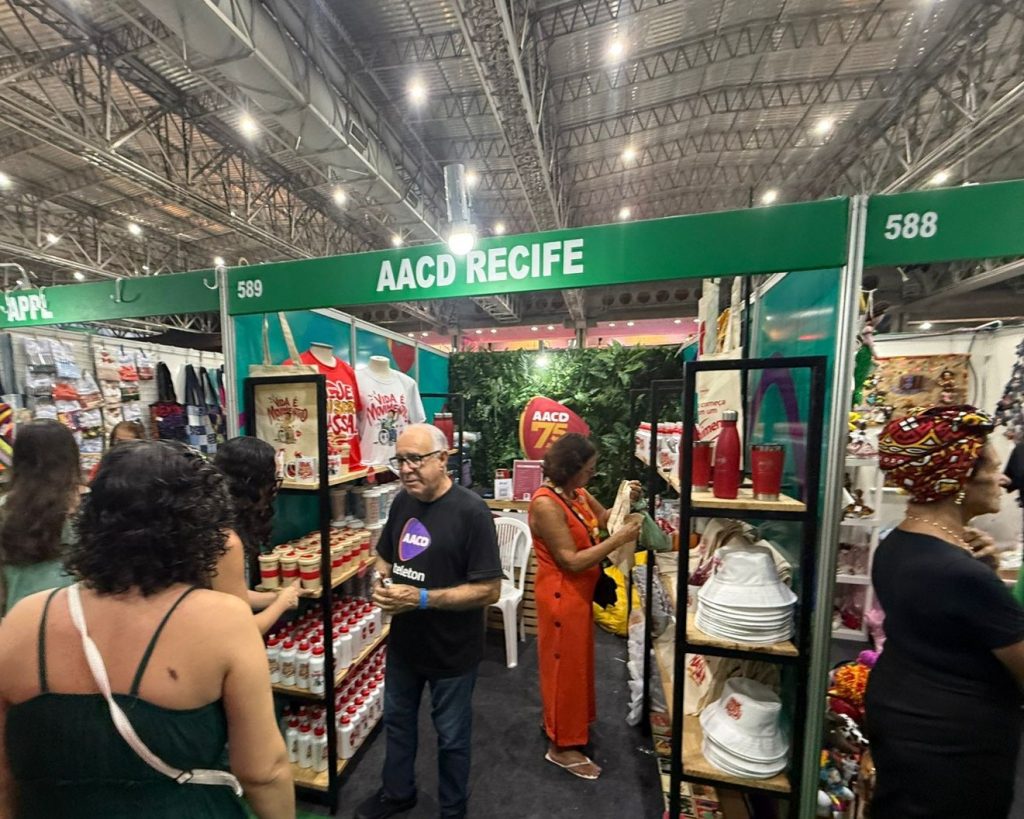 Pessoas dentro do estande da AACD Recife vendo os produtos ilustrados pelo artista Véio Art na Fenearte 2025.