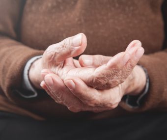 pessoa idosa de pele branca segurando nas próprias mãos. Um dos sintomas do Parkinson são os tremores continuos. Fisioterapia é uma das especialidades da AACD.
