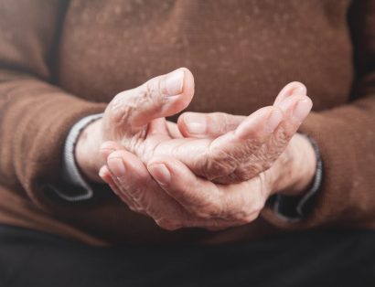 Pessoa idosa de pele branca segurando nas próprias mãos. Um dos sintomas do Parkinson.