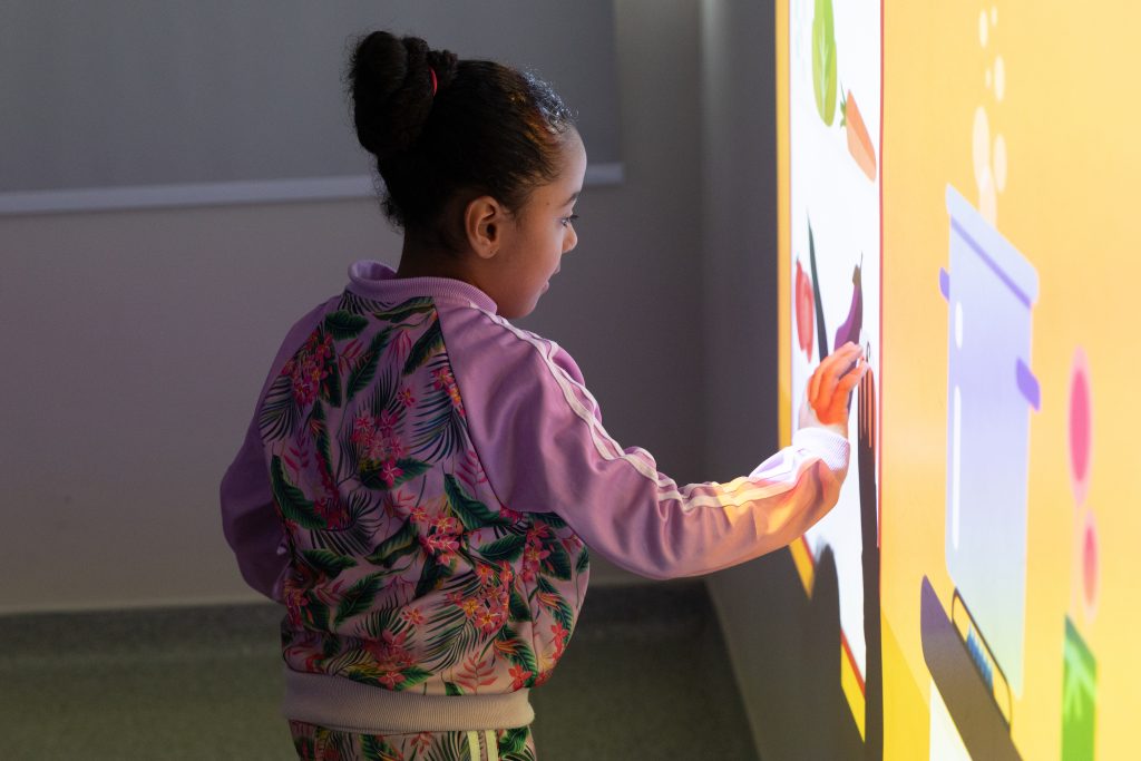 Menina interage com desenhos coloridos projetados em uma parede da AACD.