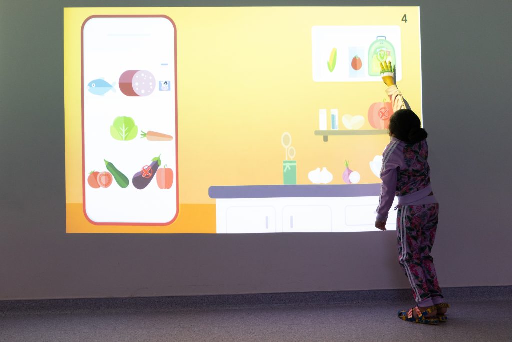 Criança toca no alto em painel de realidade virtual na parede.