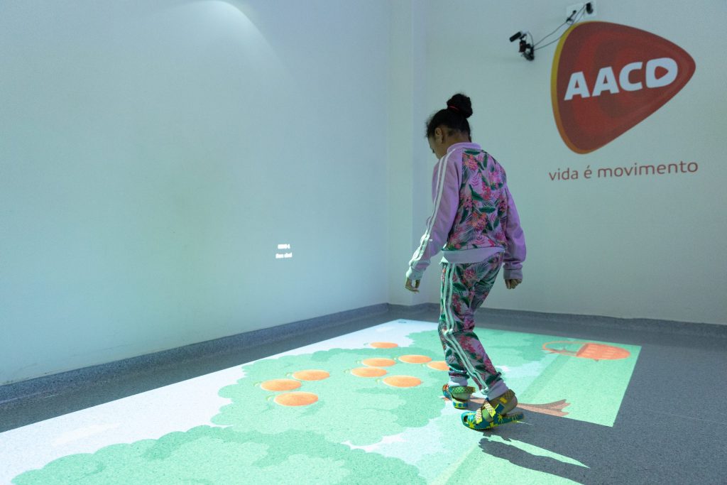 Criança pisa em panel com desenhos de realidade virtual no chão.