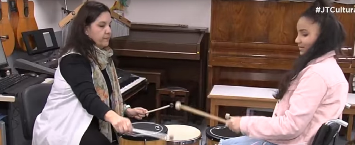 Terapeuta e menina em cadeira de rodas mexem em instrumentos musicais