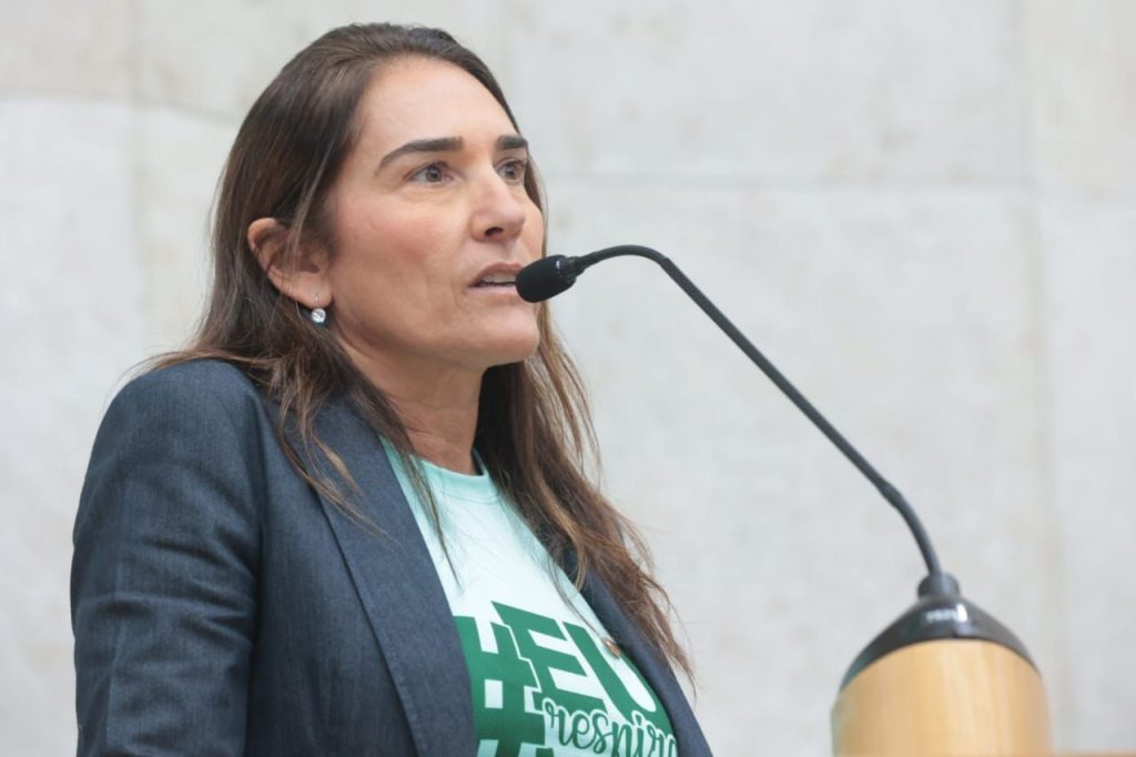 A Dra. Ana Beatriz Proença Tarran, fisiatra da AACD, palestra sobre Asfixia Perinatal. Ela é uma mulher branca, cabelos castanhos claros longos e veste a camiseta verde da campanha com um blazer cinza escuro por cima.