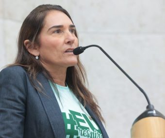 A Dra. Ana Beatriz Proença Tarran, fisiatra da AACD, palestra sobre Asfixia Perinatal. Ela é uma mulher branca, cabelos castanhos claros longos e veste a camiseta verde da campanha com um blazer cinza escuro por cima.