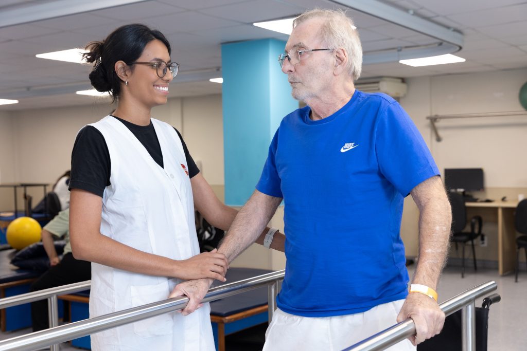 Pessoa com deficiência segura barras e interage com fisioterapeuta como parte da sua reabilitação na AACD