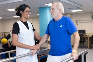 Pessoa com deficiência segura barras e interage com fisioterapeuta como parte da sua reabilitação na AACD