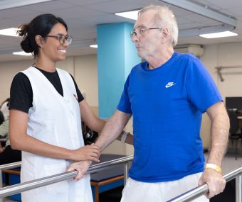 Pessoa com deficiência segura barras e interage com fisioterapeuta como parte da sua reabilitação na AACD