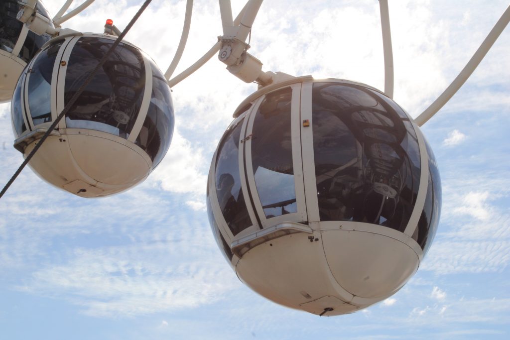 Cabine da roda gigante em destaque. Atrás vesse céu azul com poucas nuvens.