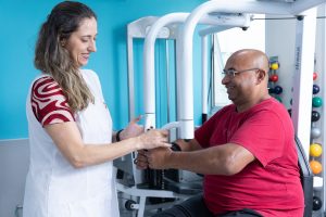 Profissional acompanha paciente durante exercício de fortalecimento dos membros superiores.