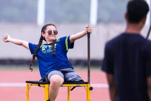 Atleta sentada em cadeira de arremesso realiza lançamento de bola durante treino de atletismo paralímpico