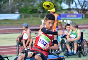 Atleta em cadeira de lançamento arremessa disco durante competição de atletismo paralímpico