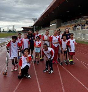 Grupo de atletas da AACD Esportes reunido e uniformizado na pista de atletismo do Centro Paralímpico Brasileiro