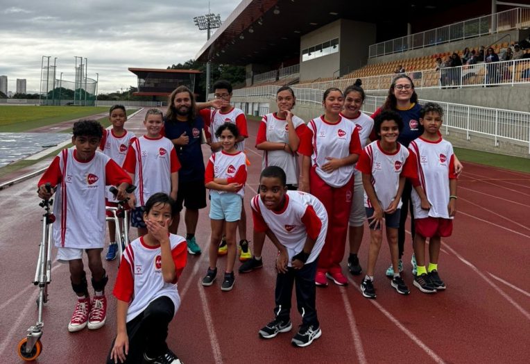 Grupo de atletas da AACD Esportes reunido e uniformizado na pista de atletismo do Centro Paralímpico Brasileiro