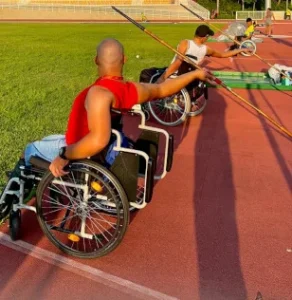 Atletas em cadeiras de corrida se posicionam lado a lado para provas de lançamento na pista de atletismo
